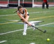 Female field hockey player in action, striking ball on turf field during a competitive match.