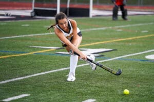 Female field hockey player in action, striking ball on turf field during a competitive match.