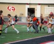 Girls' field hockey match in action, players competing near the goal on a vibrant green field.