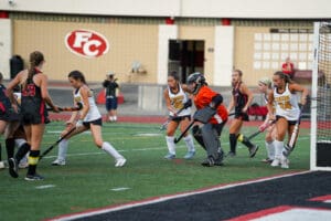 Girls' field hockey match in action, players competing near the goal on a vibrant green field.