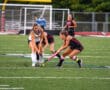 Girls playing intense field hockey match on a green turf field, competing for the ball.