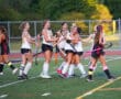 High school field hockey team celebrating a victory with teammates hugging on the field.