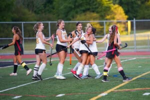 High school field hockey team celebrating a victory with teammates hugging on the field.