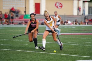Two field hockey players compete for the ball on a green turf field during a match.