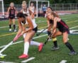 Field hockey players in action during a competitive match on a grassy field.