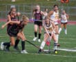 Girls playing competitive field hockey, focusing on a player in black defending against a player in white with the ball.