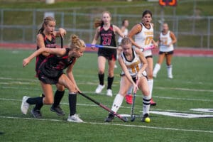 Girls playing competitive field hockey, focusing on a player in black defending against a player in white with the ball.