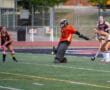 Girls' field hockey match with goalie defending and players in action on the field.