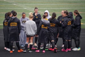 Field hockey team huddling on a field, wearing North Allegheny jackets, ready for a game.