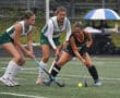 High school field hockey game with three players competing for the ball on a rainy day.