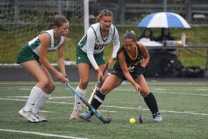 High school field hockey game with three players competing for the ball on a rainy day.