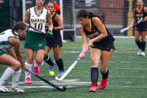 Girls' field hockey match with players in action, focusing on passing and teamwork.