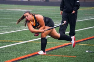 Field hockey player in action, focused during match on a green turf field, wearing a black uniform.