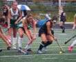 Field hockey players compete for the ball on a rainy day.