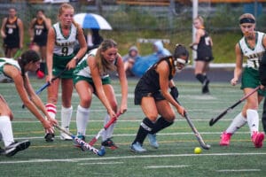 Field hockey players compete for the ball on a rainy day.