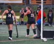 Field hockey game in action as players in black uniforms prepare near the goal, focus on teamwork and strategy.