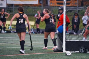 Field hockey game in action as players in black uniforms prepare near the goal, focus on teamwork and strategy.