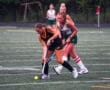 Two female field hockey players compete for the ball on a grassy field during a match.
