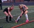 Two female field hockey players competing for the ball on a turf field during a match.