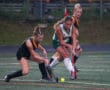 Girls playing field hockey in rain, focus on action and teamwork on wet turf.