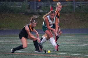 Girls playing field hockey in rain, focus on action and teamwork on wet turf.