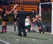 Field hockey team celebrating a scored goal with excitement near the goalpost.