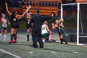 Field hockey team celebrating a scored goal with excitement near the goalpost.