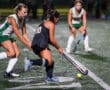 Field hockey players in action, focusing on controlling a yellow ball under stadium lights.