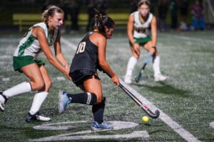 Field hockey players in action, focusing on controlling a yellow ball under stadium lights.