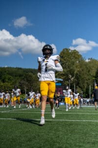 Football player in yellow and white uniform jogging on a field, clear blue sky background.