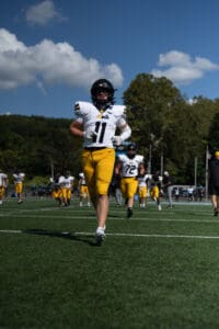 Football players in yellow and white uniforms running on a sunny field during a game.