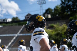 Football player in uniform and helmet with paw logo, standing on field during a sunny day practice.