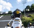Football player in helmet with a paw logo on a sunny day at a stadium, teammates blurred in the background.