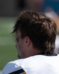 Rear view of a football player on field wearing a white jersey with a yellow and black stripe.