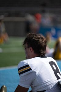 Football player wearing number 8 jersey sitting on the sidelines during a sunny game.