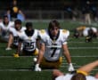 Football players stretch on a field in team practice, wearing yellow and white uniforms.
