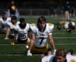 Football team players doing stretches on the field in yellow and black uniforms before practice.