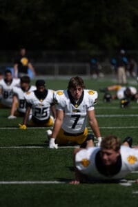 Football team players doing stretches on the field in yellow and black uniforms before practice.