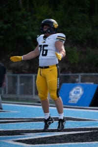 Football player in uniform standing on field during a game, arms outstretched.