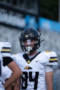 Football player in black helmet and white jersey with number 84 during a game on a field.