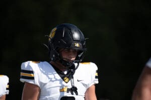 Football player in black helmet and white jersey focuses intensely on the field during a game.