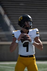 Football player in yellow pants preparing to pass the ball on a sunny field.