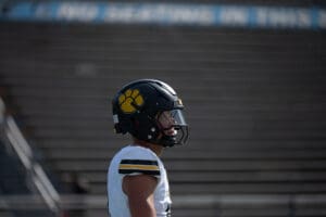 Football player in helmet with paw logo stands on empty stadium seats background.