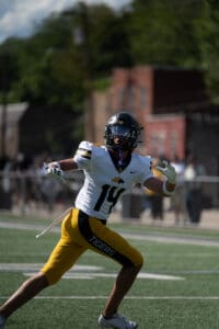 American football player in white and yellow uniform runs on field during daytime game.