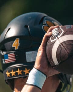 Football player in helmet preparing to throw a football, close-up on hand and helmet with number 4 and flag sticker.
