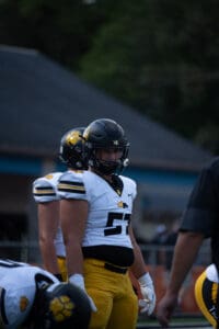 Football players wearing black helmets and yellow pants during a game, focused and ready on the field.