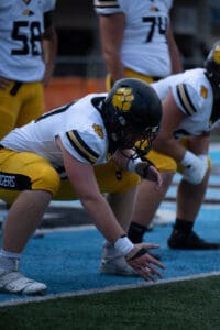 Football players in yellow uniforms crouch on the field, preparing for a play.