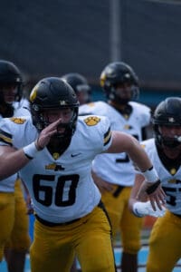 Football players in black and yellow uniforms practicing on a field, focus on number 60.
