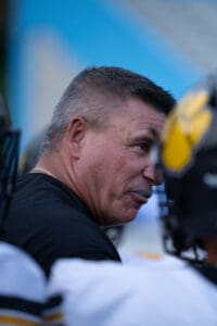 Football coach speaking to players on the sidelines during a game, focused and engaged.