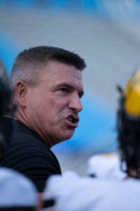 Man coaching a football team, talking passionately on the sideline during a game.